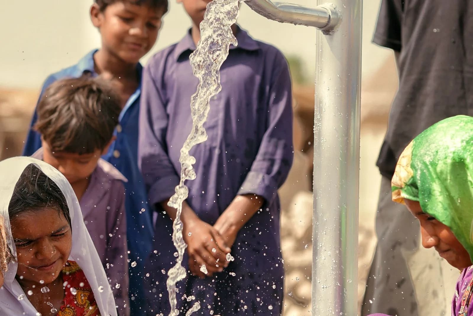A hand-operated water pump being used in an outdoor community setting.