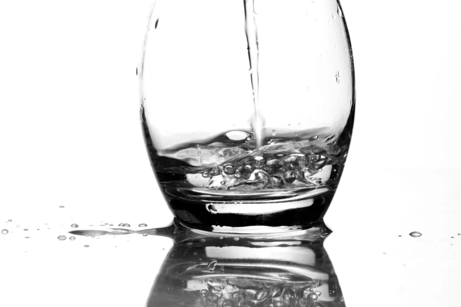 Clear water pouring into a glass on a bright background.