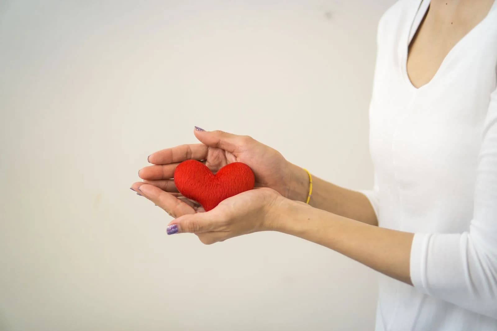 Hands gently holding a small red heart symbol.